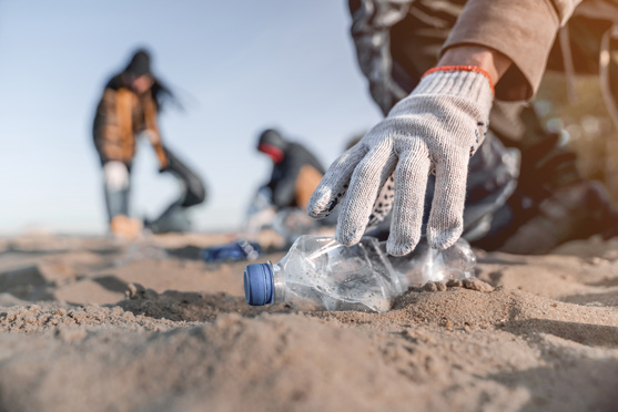 image of gloved hand picking up bottle on a sandy beach