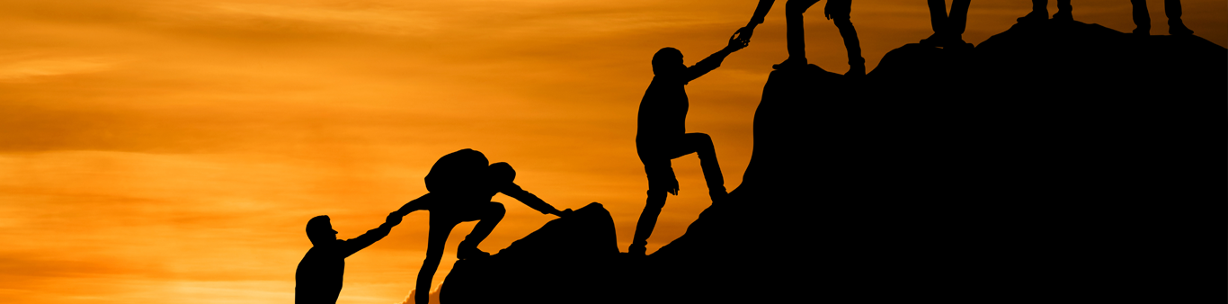 silhouetted image of people helping each other up a mountain