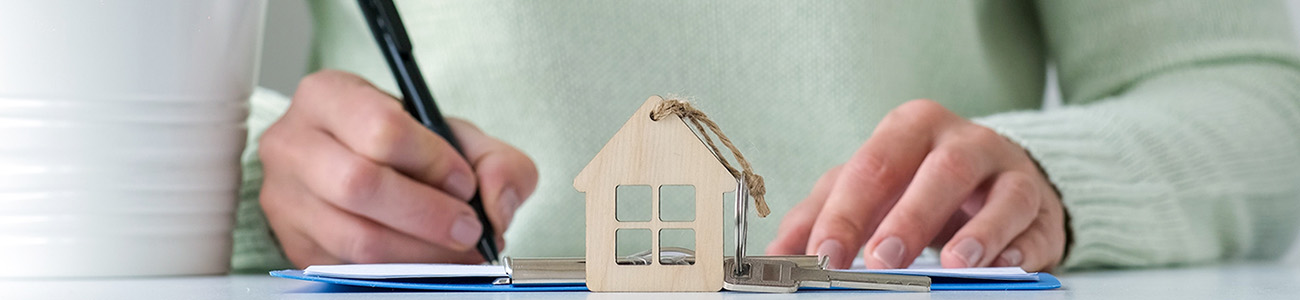 woman writing on paper behind a miniature house keychain