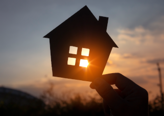 hand holding templated shape of home over a sunset